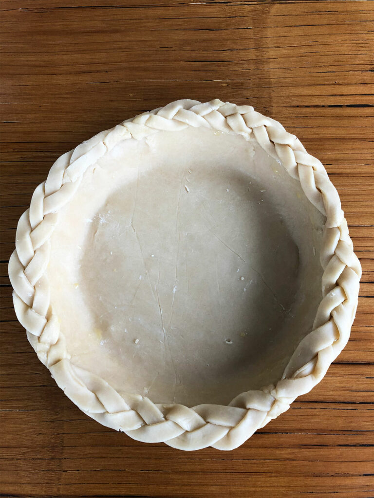 Brush the rim of the crust with egg wash and apply braids to the top.